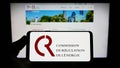 Person holding smartphone with logo of French Commission de Regulation de l\'Energie (CRE) on screen.