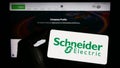 Person holding smartphone with logo of French company Schneider Electric SE on screen in front of website. Royalty Free Stock Photo