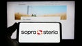 Person holding smartphone with logo of French company Sopra Steria Group SA on screen in front of website.