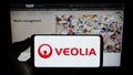 Person holding smartphone with logo of French company Veolia Environnement S.A. on screen in front of website.