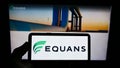 Person holding smartphone with logo of French facility management company EQUANS on screen in front of website.