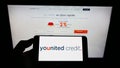 Person holding smartphone with logo of French financial platform company Younited Credit on screen in front of website.