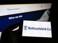 Person holding smartphone with logo of French financial services company Rothschild Co. SCA on screen in front of website.