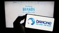 Person holding smartphone with logo of French food company Danone S.A. on screen in front of website.