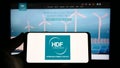 Person holding smartphone with logo of French hydrogen company HDF Energy on screen in front of website.