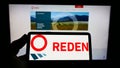 Person holding smartphone with logo of French photovoltaic company Reden Solar S.A.S. on screen in front of website.