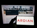 Person holding smartphone with logo of French private equity company Ardian on screen in front of website.