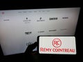 Person holding smartphone with logo of French spirits company RÃÂ©my Cointreau S.A. on screen in front of website. Royalty Free Stock Photo