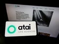 Person holding smartphone with logo of German biotech company ATAI Life Sciences AG on screen in front of website.