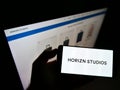 Person holding smartphone with logo of German company Horizn Studios (HS New Travel GmbH) on screen in front of website.