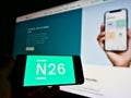 Person holding smartphone with logo of German direct bank N26 with website in background.