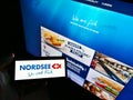 Person holding smartphone with logo of German fast-food restaurant chain Nordsee GmbH on display in front of business website.