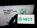 Person holding smartphone with logo of German identity verification company Nect GmbH on screen in front of website. Royalty Free Stock Photo