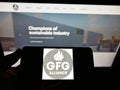 Person holding smartphone with logo of Gupta Family Group Alliance (GFG Alliance) on screen in front of website.