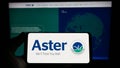 Person holding smartphone with logo of health company Aster DM Healthcare Limited on screen in front of website.