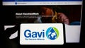 Person holding smartphone with logo of health partnership Gavi, the Vaccine Alliance on screen in front of website.