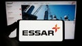 Person holding smartphone with logo of Indian conglomerate Essar Group on screen in front of website.