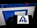 Person holding smartphone with logo of Indian conglomerate ITC Limited on screen in front of website.