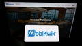 Person holding smartphone with logo of Indian financial technology company MobiKwik on screen in front of website.