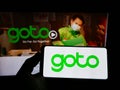 Person holding smartphone with logo of Indonesian company GoTo Group on screen in front of website.