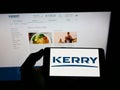 Person holding smartphone with logo of Irish food company Kerry Group plc on screen in front of website.