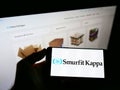 Person holding smartphone with logo of Irish packaging company Smurfit Kappa Group plc on screen in front of website. Royalty Free Stock Photo