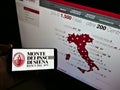 Person holding smartphone with logo of Italian bank Banca Monte dei Paschi di Siena (BMPS) on screen with website.