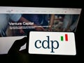 Person holding smartphone with logo of Italian bank Cassa Depositi e Prestiti SpA (CDP) on screen in front of website.