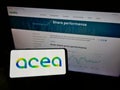 Person holding smartphone with logo of Italian utility company Acea S.p.A. on screen in front of website.