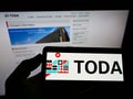 Person holding smartphone with logo of Japanese construction company Toda Corporation on screen in front of website.