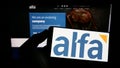 Person holding smartphone with logo of Mexican company Alfa S.A.B. de C.V. on screen in front of website.