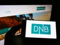 Person holding smartphone with logo of Norwegian financial services company DNB ASA on screen in front of website.