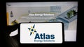 Person holding smartphone with logo of oil and gas company Atlas Energy Solutions Inc. on screen in front of website.