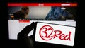 Person holding smartphone with logo of online casino company 32Red Limited on screen in front of website.