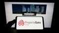 Person holding smartphone with logo of online property company PropertyGuru Pte. Ltd. on screen in front of website.