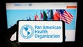 Person holding smartphone with logo of Pan American Health Organization (PAHO) on screen in front of website. Royalty Free Stock Photo