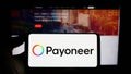 Person holding smartphone with logo of payments company Payoneer Global Inc. on screen in front of website.