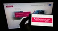 Person holding smartphone with logo of Polish financial company Bank Millennium S.A. on screen in front of website.