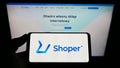 Person holding smartphone with logo of Polish software company Shoper S.A. on screen in front of website.