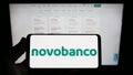 Person holding smartphone with logo of Portuguese banking company Novo Banco S.A. on screen in front of website.