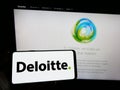 Person holding smartphone with logo of professional services company Deloitte on screen in front of website.