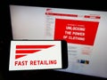 Person holding smartphone with logo of retail company K.K. Fast Retailing on screen with website.