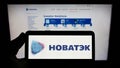 Person holding smartphone with logo of Russian natural gas company Novatek on screen in front of website.