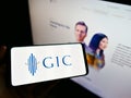 Person holding smartphone with logo of Singaporean sovereign wealth fund GIC Private Limited on screen in front of website.