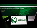 Person holding smartphone with logo of South African bank Nedbank Group Limited on screen in front of website.