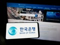 Person holding smartphone with logo of South Korean central bank Bank of Korea (BOK) on screen in front of website.