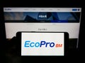 Person holding smartphone with logo of South Korean company Ecopro BM Co. Ltd. on screen in front of website.