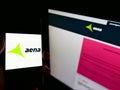 Person holding smartphone with logo of Spanish airport operator Aena S.A. on screen in front of website.