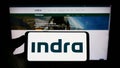 Person holding smartphone with logo of Spanish company Indra Sistemas S.A. on screen in front of website.