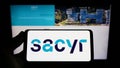 Person holding smartphone with logo of Spanish infrastructure company Sacyr S.A. on screen in front of website.